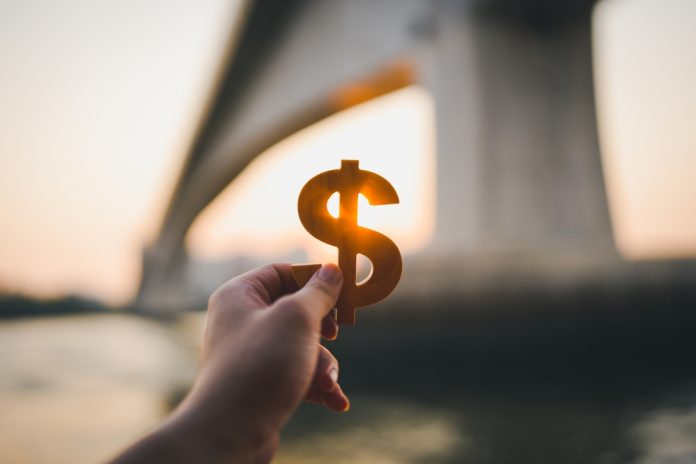 hand holding a Dollar sign with blurry bridge